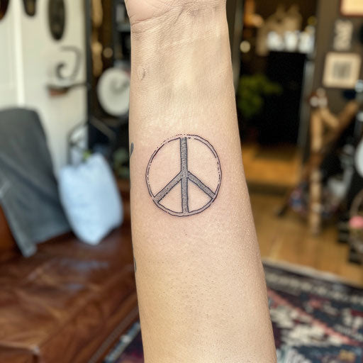 Simple peace sign tattoo, in the style of Guy Aitchison, on the forearm