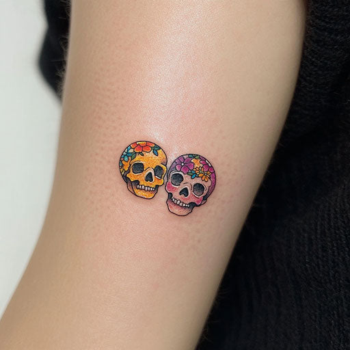 Small matching tattoos of tiny skulls in the style of Ed Hardy