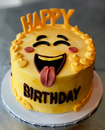 Yellow cake with winking emoji and sticking out tongue, HAPPY BIRTHDAY