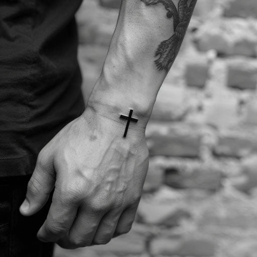 Minimalist wrist tattoos for men featuring a cross, Ami James style